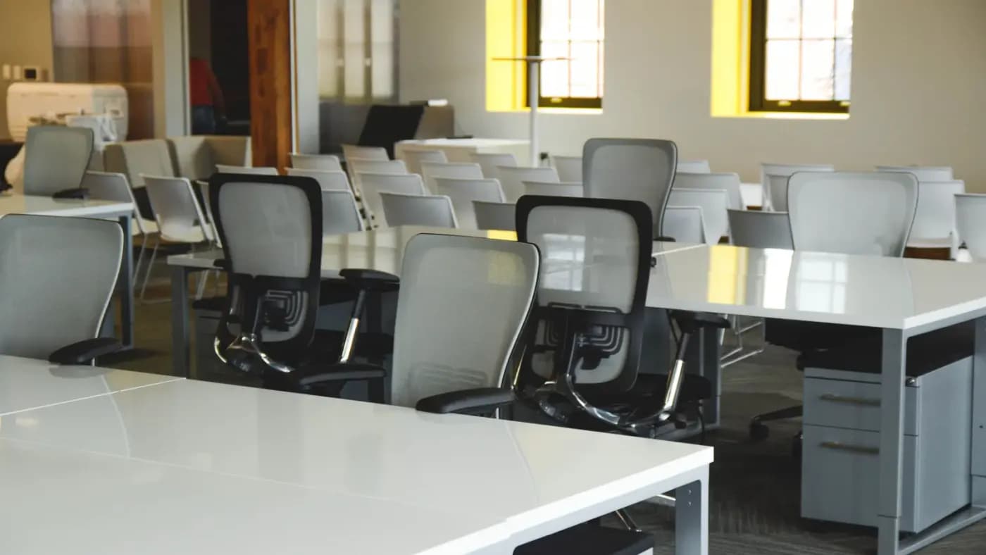 Ortak çalışma alanında sıralanmış boş çalışma masaları ve ofis koltukları